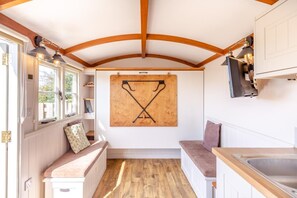 A compact kitchen with wooden beams, a wooden floor, a corkboard with hooks, and a bench with cushions. - 1 Bed in St Austell (oc-h45926) (High Street)