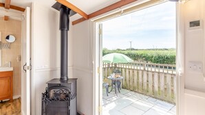 Una habitación con estufa de leña, una puerta de madera, una mesita con una silla y vistas a un viñedo a través de una puerta abierta.