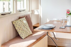 A dining area with a bench, a table set with plates, a glass, and a vase with flowers. - 1 Bed in St Austell (oc-h45926) (High Street)