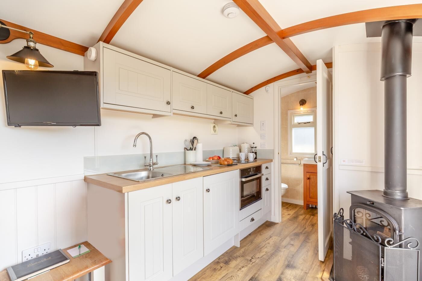 A compact kitchen with white cabinetry, a built-in oven, and a wood-burning stove.