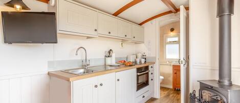 A compact kitchen with white cabinetry, a built-in oven, and a wood-burning stove.