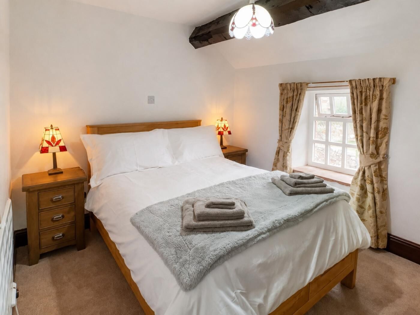 Een slaapkamer met een houten bed, twee bedlampen, een raam met gordijnen en een radiator.
