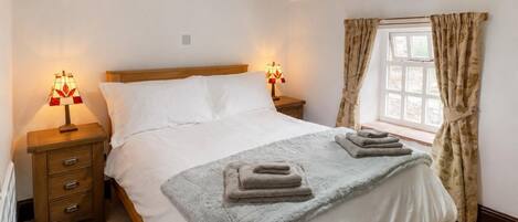 Een slaapkamer met een houten bed, twee bedlampen, een raam met gordijnen en een radiator.