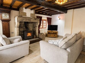 Ein gemütliches Wohnzimmer mit Kamin aus Stein, Holzbalken, einem Fernseher und zwei Sofas.