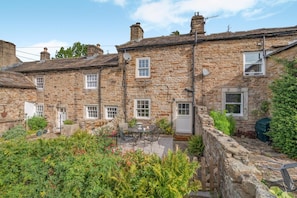 A stone building with multiple windows and a small garden area with a table and chairs. - 1 Bed in Gunnerside (oc-m45922) (Gunnerside)