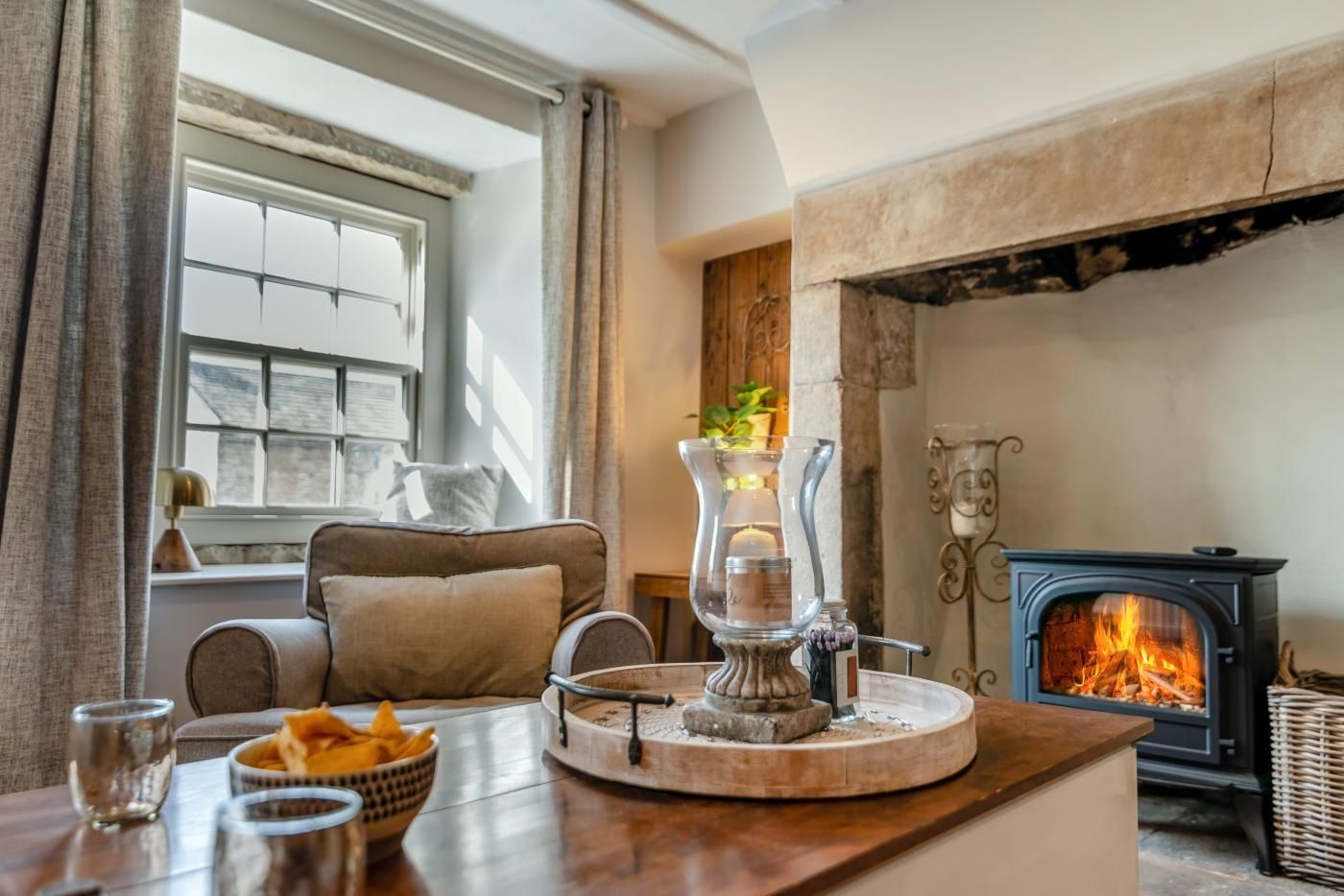 Una sala de estar acogedora con chimenea, un sofá cómodo, una mesa con aperitivos y un ventanal con cortinas.