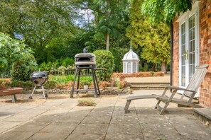 Eine Terrasse mit Grill, ein Pavillon und ein Backsteinhaus.