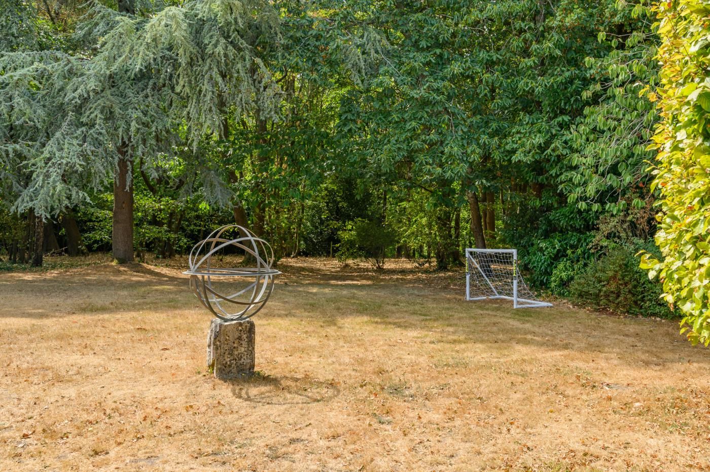 A park with a metal sculpture, a soccer goal, and dense greenery.