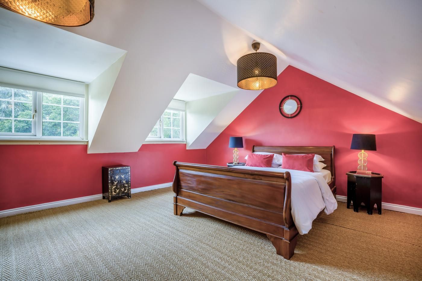 A bedroom with a sloped ceiling, a bed with pillows, two bedside tables with lamps, and a window.