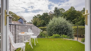 Une terrasse avec une petite table et des chaises, entourée d’une clôture en métal et d’une végétation luxuriante.