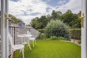 Eine Terrasse mit einem kleinen Tisch und Stühlen, umgeben von einem Metallzaun und üppigem Grün.
