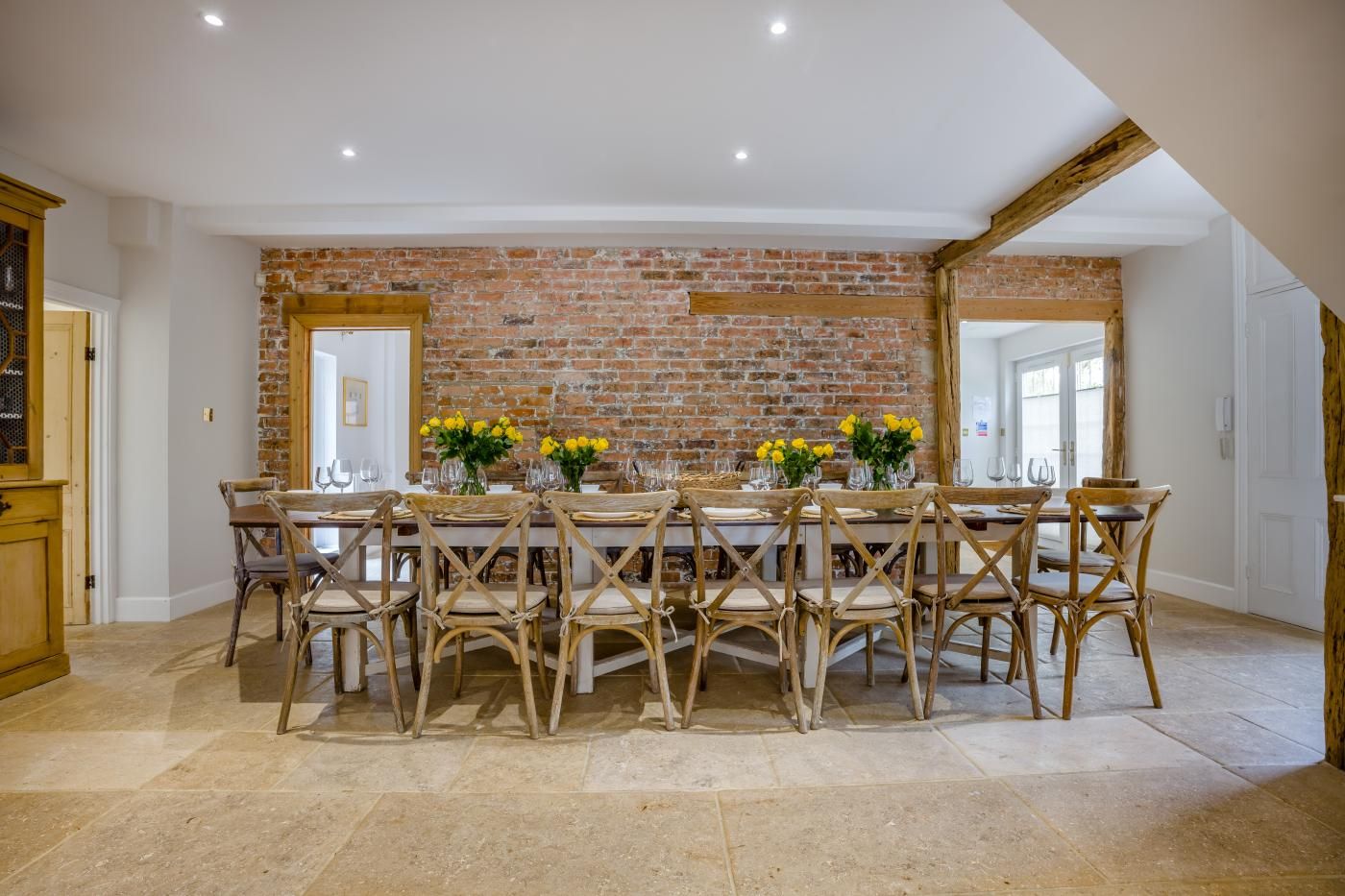 A dining area with a brick wall, wooden chairs, and a table set for six.