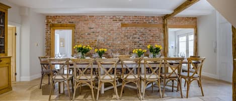 A dining area with a brick wall, wooden chairs, and a table set for six.