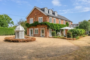 A brick house with a covered patio and a small garden. - 8 Bed in Wimborne (oc-w45946) (Bournemouth)