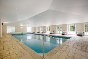 An indoor swimming pool with a tiled floor, a metal pool ladder, and multiple seating areas with cushions. - 8 Bed in Wimborne (oc-w45946) (Bournemouth)