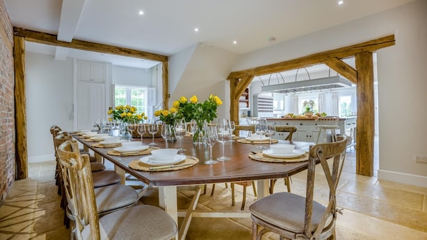 Un espace repas avec une longue table dressée pour un repas, entourée de chaises en bois.