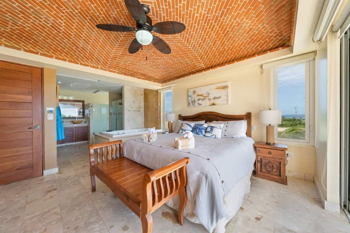 Un dormitorio con techo de ladrillo, una cama, una mesita de noche, un banco de madera y vistas al exterior.