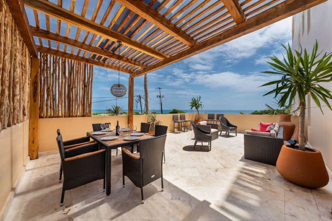 An outdoor patio with a wooden pergola, wicker furniture, and a view of the ocean.