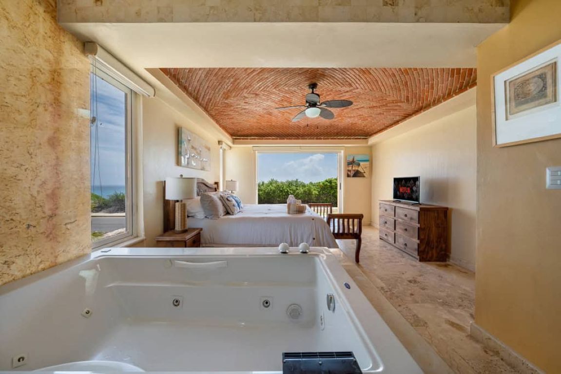 Une chambre dotée d’une grande baignoire, d  ’un lit, d’une télévision et offrant une vue sur l’extérieur.