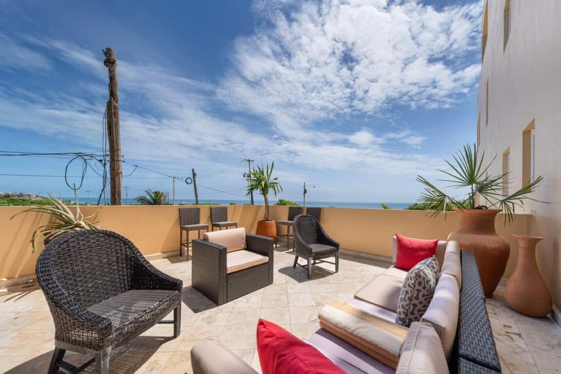 Eine Terrasse mit Gartenmöbeln, Blick auf das Meer und ein Gebäude im Hintergrund.