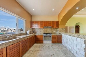 A kitchen with granite countertops, wooden cabinets, a stainless steel range, and a window overlooking a cityscape. - Luxury Oceanfront 2-Bedroom Condo at Isla 33 (Isla Mujeres)