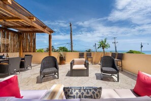 Eine Terrasse mit Korbmöbeln, einer Holz-Pergola und Blick auf den Ozean.