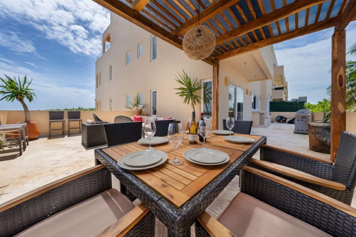 Un espacio de comedor al aire libre con mobiliario de mimbre y una mesa de madera dispuesta para dos personas.