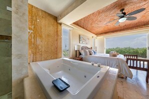 A bedroom with a large bathtub, a bed, a ceiling fan, and a view of the outdoors.