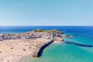 An aerial view of a coastal town with a beach, a fortified structure, and a hilltop with buildings. - 4 Bed in St. Ives (oc-s46007) (Saint Ive)