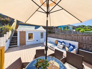 A covered outdoor seating area with a table and chairs, a small building with a window, and a wooden deck. - 4 Bed in St. Ives (oc-s46007) (Saint Ive)