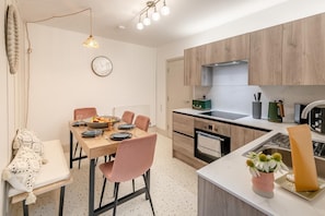 A modern kitchen with wooden cabinets, a dining table with pink chairs, and a built-in oven. - 4 Bed in St. Ives (oc-s46007) (Saint Ive)