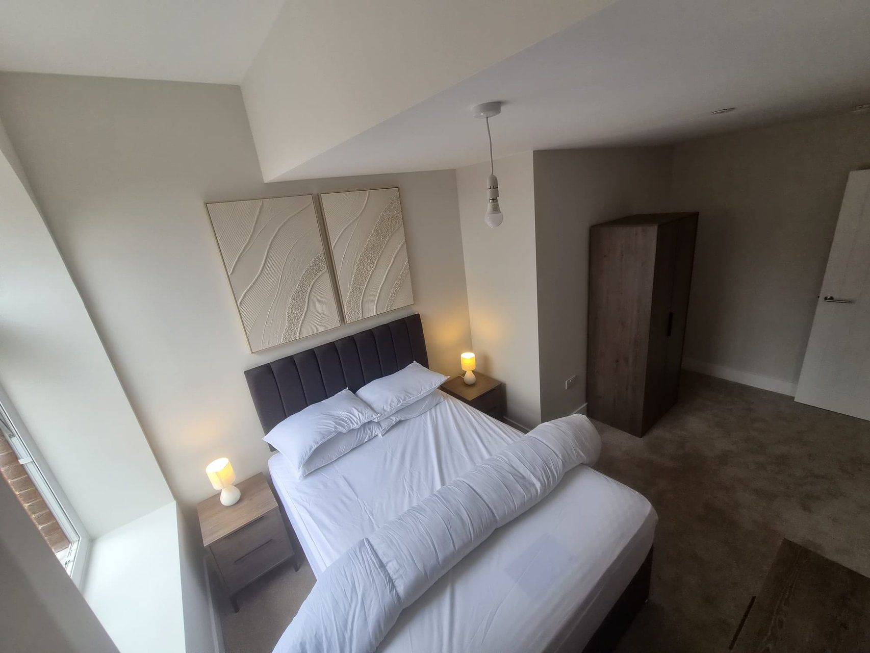 A modern bedroom with a large bed, two bedside tables with lamps, a wardrobe, and a ceiling light fixture.