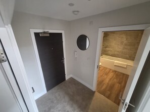 Ein Flur mit Teppichboden, einer Tür mit schwarzem Rahmen und einem Spiegel an der Wand.