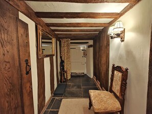Ein schmaler Korridor mit Holzbalken, einer Bank, einem Spiegel und einer Tür.