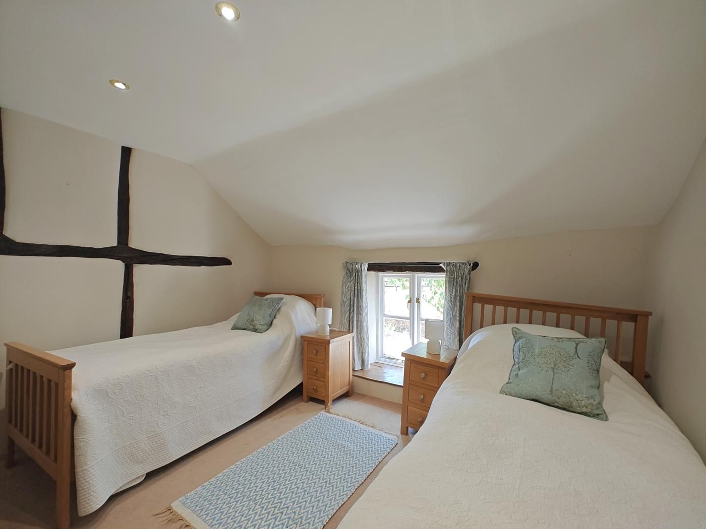 A bedroom with two single beds, a wooden headboard, a nightstand, and a window with curtains.