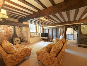 Ein rustikales Wohnzimmer mit freiliegenden Holzbalken, einer Steinwand, einem Kamin und einem Fernseher.