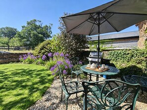 Eine Terrasse mit einem runden Tisch, Stühlen, einem Grill und einem großen Sonnenschirm.