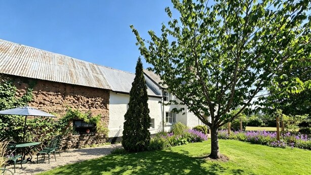 A rustic building with a stone wall and a white house with a sloped roof. - 2 Bed in Buckerell (oc-h45977) (Buckerell)