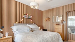 Ein Schlafzimmer mit einem Bett, Nachttischen, einem Schminktisch, einem Spiegel und einer Wandleuchte.