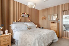 Ein Schlafzimmer mit einem Bett, Nachttischen, einem Schminktisch, einem Spiegel und einer Wandleuchte.