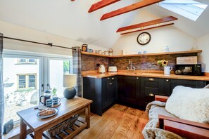 Een kleine keuken met een houten aanrecht, zwarte kastjes, een zichtbare klok en een eethoek met een tafel en stoelen.