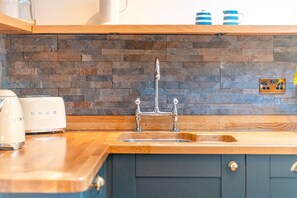 Een keuken met een stenen achterwand, een houten aanrechtblad en een dubbele spoelbak.