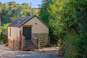 A small stone building with a dark door and steps leading up to it, surrounded by greenery. - 1 Bed in Botus Fleming (oc-f45947) (Botusfleming)