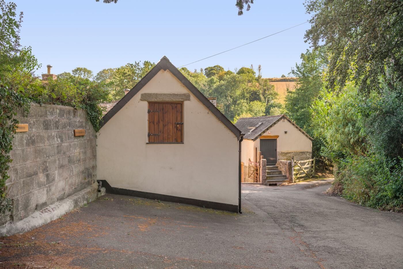 A narrow driveway leading to a small, single-story building with a pitched roof and a wooden door.