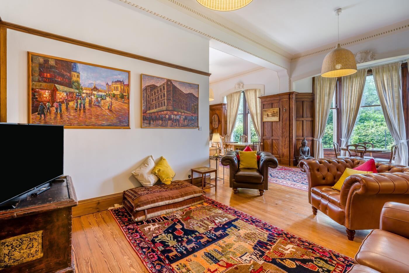 Un salon spacieux doté d’un grand téléviseur à écran plat, de canapés en cuir, d’un tapis à motifs et d’œuvres d’art représentant des scènes historiques.