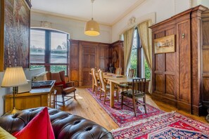 Ein Zimmer mit einem Holztisch, Stühlen, einem Ledersofa, einer Lampe und einem großen Fenster mit Jalousien.