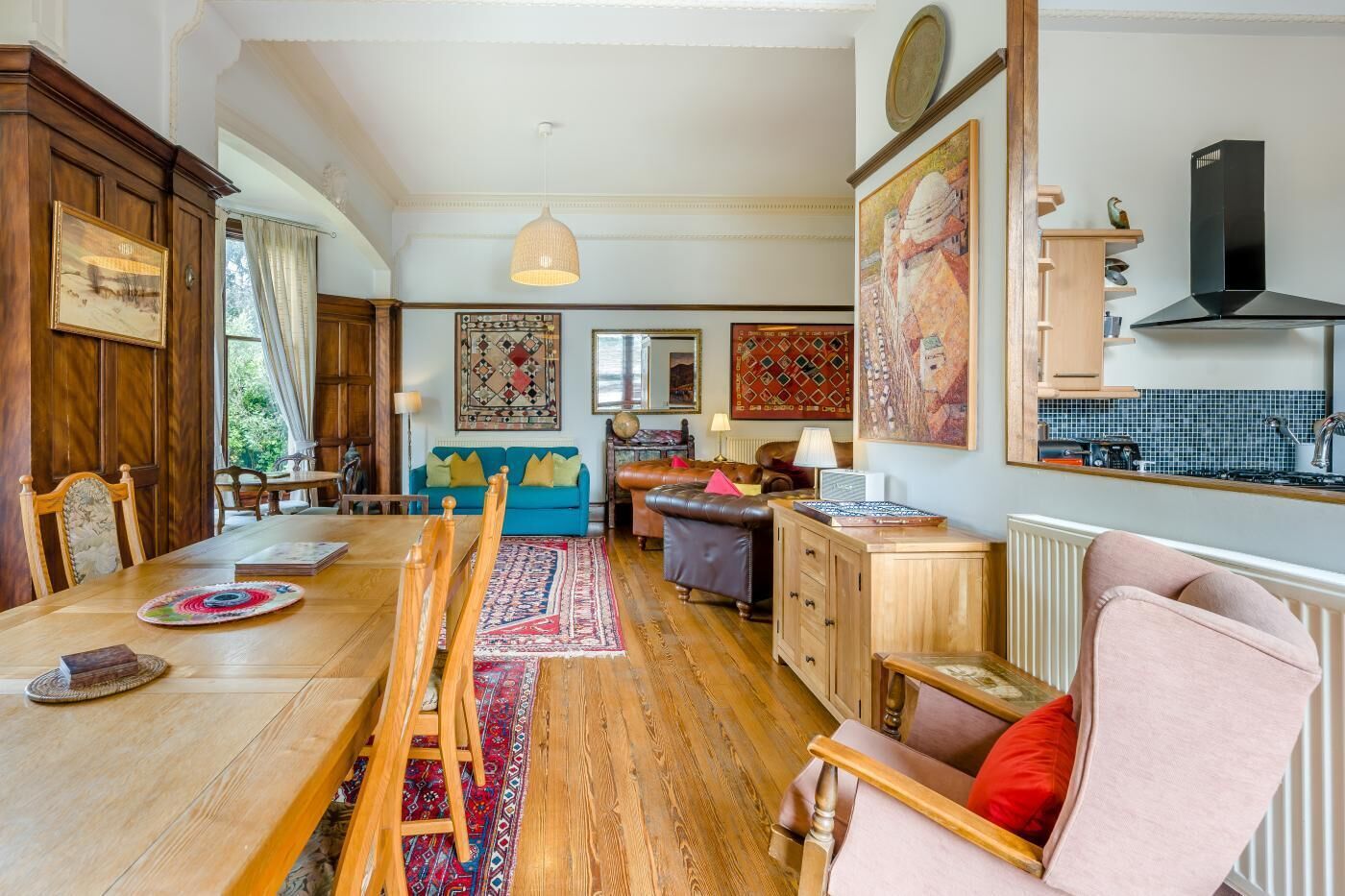 A spacious living room with a wooden dining table, a sofa, and a kitchen area visible through an open door.