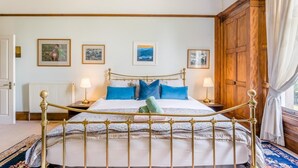 Een slaapkamer met een hemelbed, twee nachtkastjes, een radiator en ingelijste foto’s aan de muur.