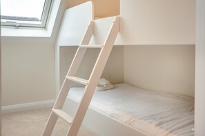 Ein Etagenbett mit einer Leiter, einem Fenster und einer weißen Wand.