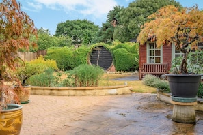 Ein Garten mit einer Holzkonstruktion, einem befestigten Bereich und verschiedenen Pflanzen.